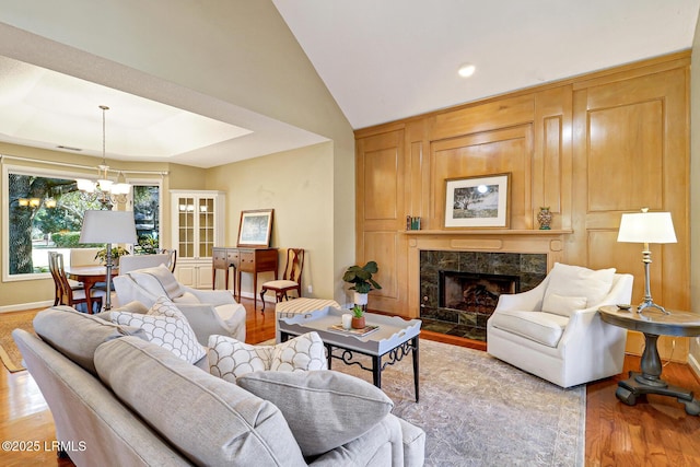 living area featuring an inviting chandelier, a high end fireplace, vaulted ceiling, wood finished floors, and baseboards