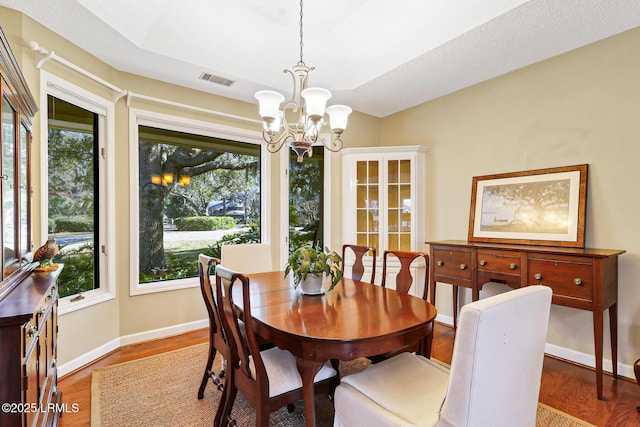 dining area featuring baseboards, wood finished floors, visible vents, and an inviting chandelier