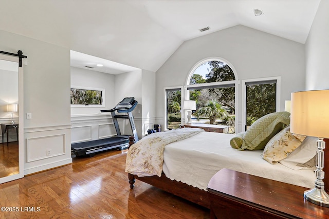 bedroom featuring lofted ceiling, visible vents, a barn door, wainscoting, and wood finished floors