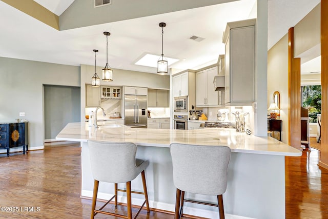 kitchen with visible vents, dark wood-type flooring, a sink, built in appliances, and a peninsula