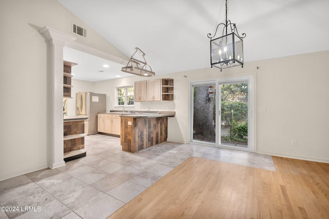 kitchen with lofted ceiling, decorative light fixtures, stainless steel fridge with ice dispenser, light brown cabinets, and kitchen peninsula