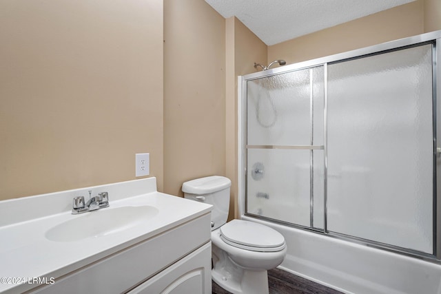 full bathroom with bath / shower combo with glass door, hardwood / wood-style flooring, vanity, toilet, and a textured ceiling