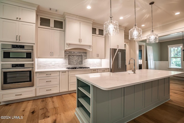 kitchen with light stone counters, pendant lighting, stainless steel appliances, a kitchen island with sink, and decorative backsplash