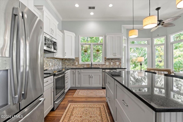 kitchen featuring crown molding, stainless steel appliances, tasteful backsplash, white cabinets, and dark stone counters