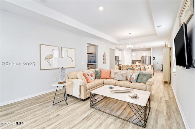 living room featuring a notable chandelier, a tray ceiling, and light wood-type flooring