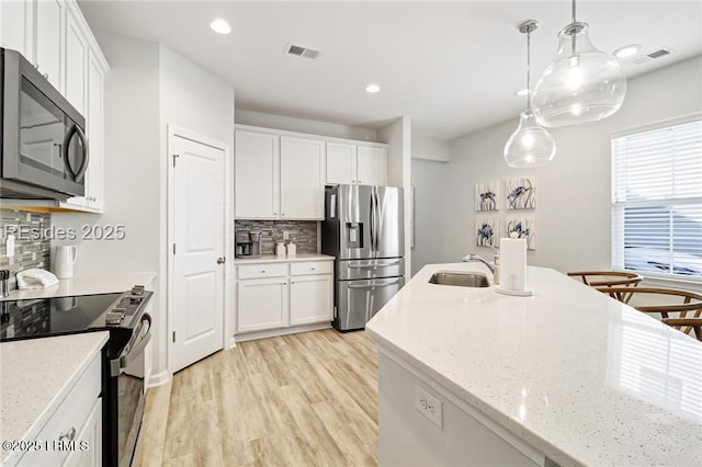 kitchen with appliances with stainless steel finishes, tasteful backsplash, sink, white cabinets, and hanging light fixtures