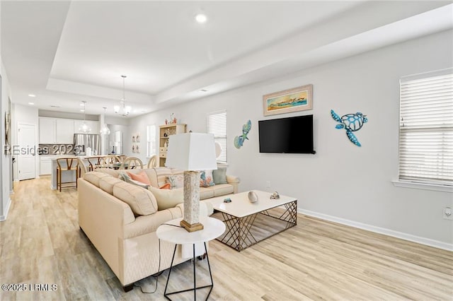 living room with a tray ceiling, a chandelier, and light hardwood / wood-style flooring