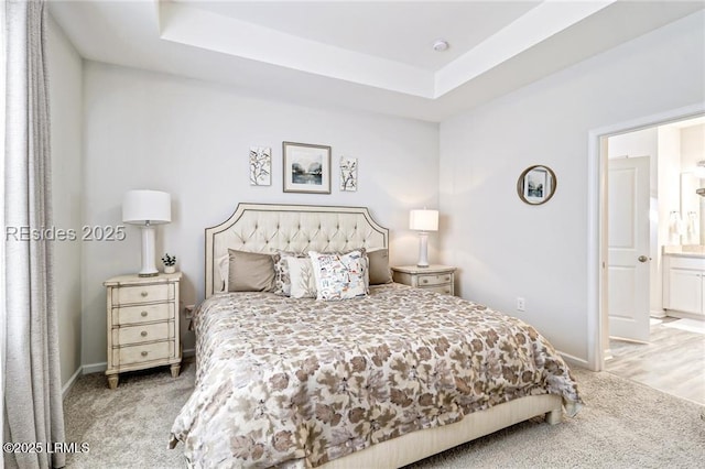 bedroom with ensuite bathroom, light carpet, and a tray ceiling