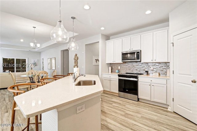 kitchen featuring sink, appliances with stainless steel finishes, white cabinetry, hanging light fixtures, and a center island with sink