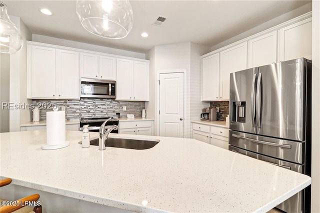 kitchen featuring appliances with stainless steel finishes, decorative light fixtures, white cabinetry, backsplash, and light stone countertops