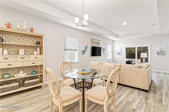dining space with a chandelier, light hardwood / wood-style floors, and a tray ceiling