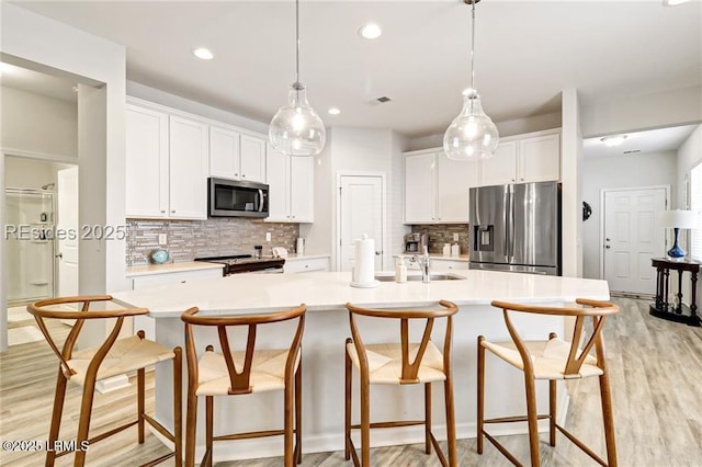 kitchen featuring pendant lighting, white cabinets, backsplash, a large island with sink, and stainless steel appliances