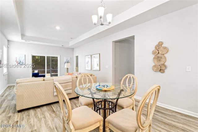 dining space featuring light hardwood / wood-style floors, a raised ceiling, and a chandelier