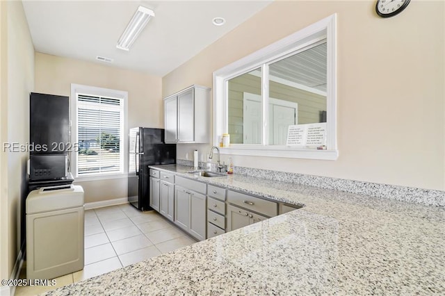 kitchen with sink, black refrigerator, light stone counters, and light tile patterned floors