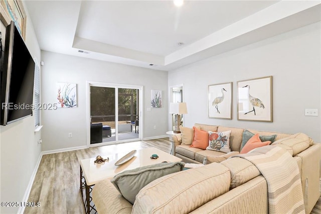 living room featuring a tray ceiling and light hardwood / wood-style floors