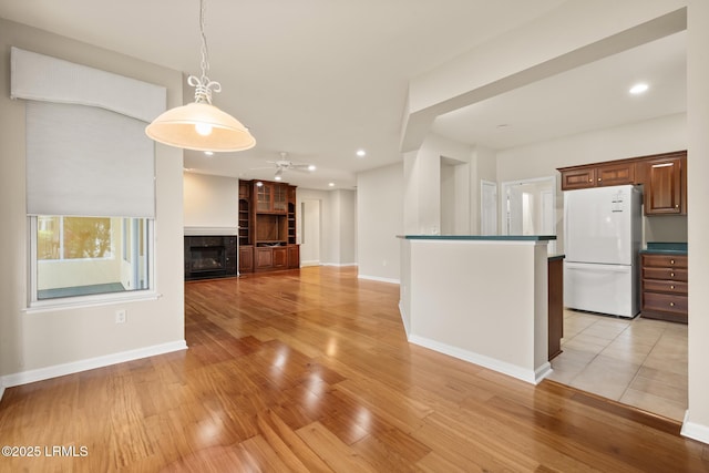 7 Fenwick Dr, Bluffton, SC 29909 - kitchen featuring freestanding refrigerator, light wood-type flooring, hanging light fixtures, a fireplace, and a ceiling fan