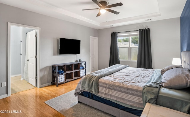 bedroom with ensuite bath, light hardwood / wood-style flooring, a raised ceiling, and ceiling fan