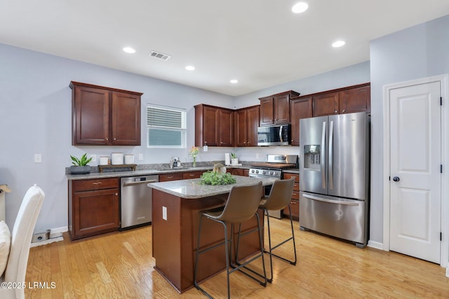 kitchen with light wood-style flooring, stainless steel appliances, a kitchen island, visible vents, and a kitchen breakfast bar