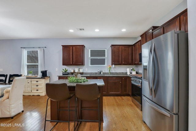 kitchen with a kitchen island, visible vents, a kitchen breakfast bar, appliances with stainless steel finishes, and light wood finished floors