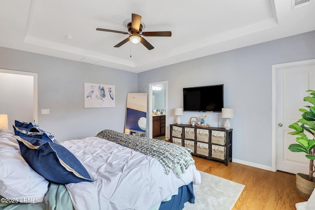 bedroom featuring a raised ceiling, visible vents, ceiling fan, wood finished floors, and baseboards