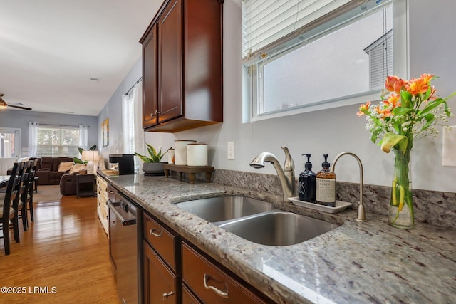 kitchen featuring light stone counters, light wood-style flooring, a sink, open floor plan, and stainless steel dishwasher