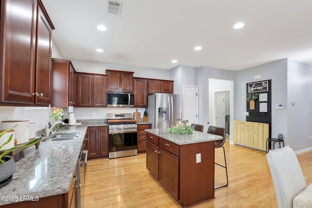 kitchen featuring visible vents, stainless steel appliances, light wood-type flooring, a kitchen bar, and a sink