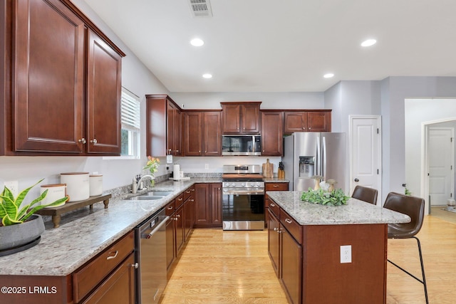 kitchen featuring a breakfast bar area, stainless steel appliances, a sink, visible vents, and light wood finished floors