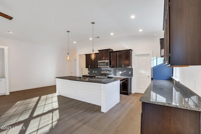 kitchen featuring light wood finished floors, dark brown cabinetry, decorative backsplash, dark stone countertops, and appliances with stainless steel finishes