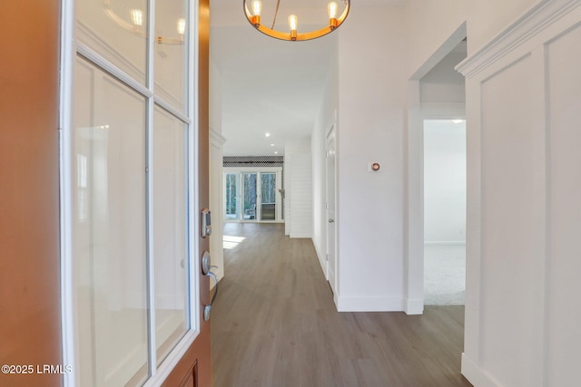 hallway featuring a chandelier, light wood-style flooring, and baseboards