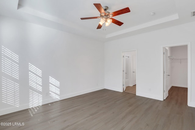 unfurnished bedroom with visible vents, a walk in closet, baseboards, a tray ceiling, and wood finished floors