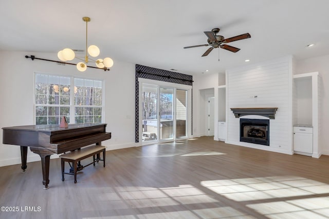 sitting room featuring baseboards, recessed lighting, ceiling fan with notable chandelier, a fireplace, and light wood-style floors