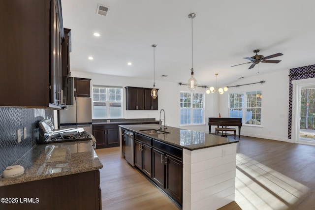 kitchen featuring light wood finished floors, dark stone countertops, dishwasher, and a sink