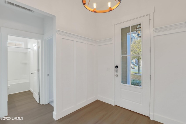 foyer entrance with visible vents, wood finished floors, an inviting chandelier, wainscoting, and a decorative wall