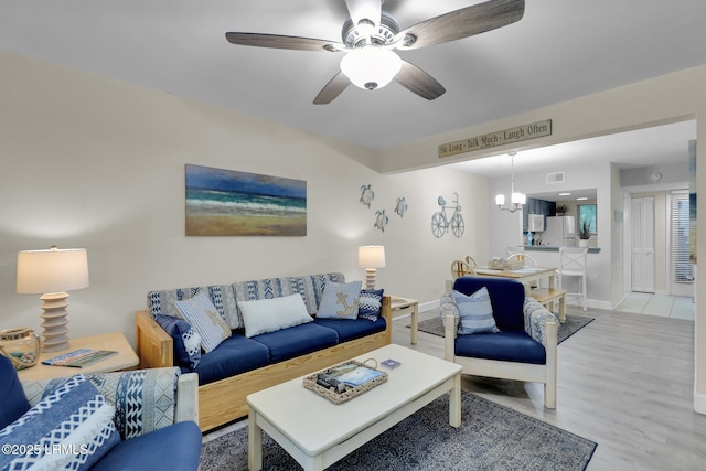 living room featuring ceiling fan with notable chandelier and light hardwood / wood-style flooring