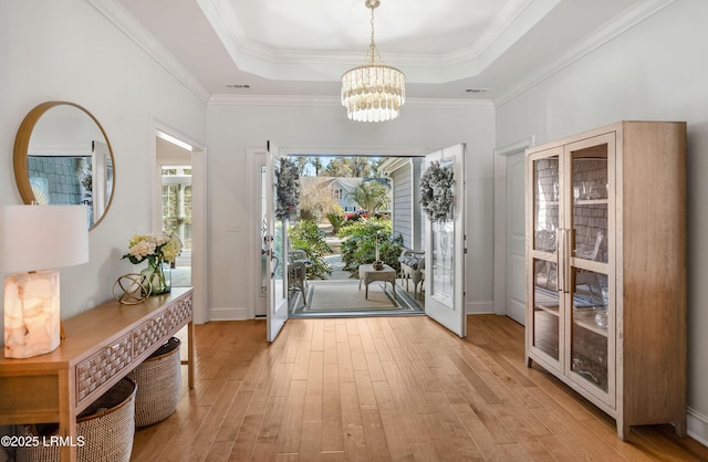 doorway with a raised ceiling, ornamental molding, a chandelier, and light wood-type flooring