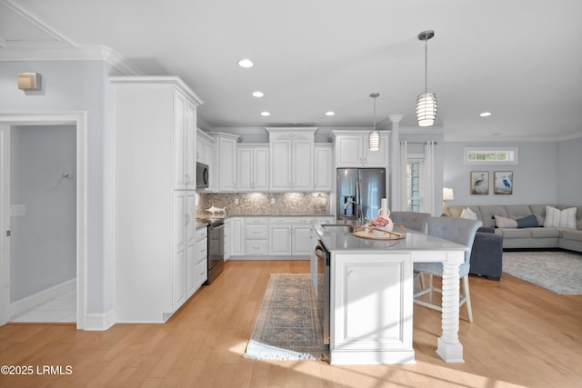 kitchen featuring a kitchen island with sink, backsplash, hanging light fixtures, stainless steel appliances, and white cabinets