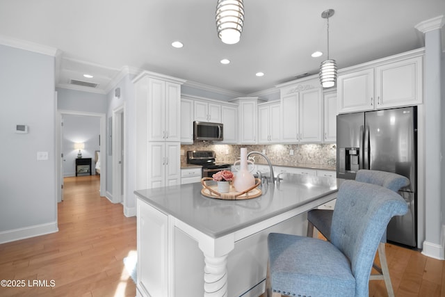 kitchen with appliances with stainless steel finishes, an island with sink, white cabinets, a kitchen breakfast bar, and hanging light fixtures