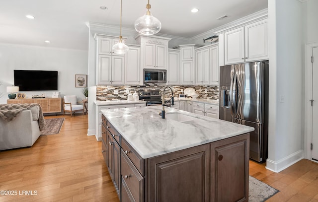 kitchen featuring stainless steel appliances, white cabinetry, hanging light fixtures, and a center island with sink