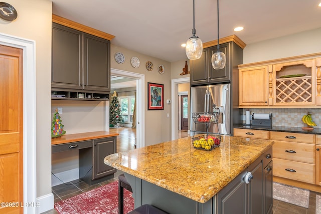 kitchen with a center island, stainless steel refrigerator with ice dispenser, built in desk, dark stone counters, and light brown cabinets