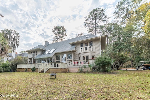 rear view of property with a balcony, an outdoor fire pit, a deck, and a lawn