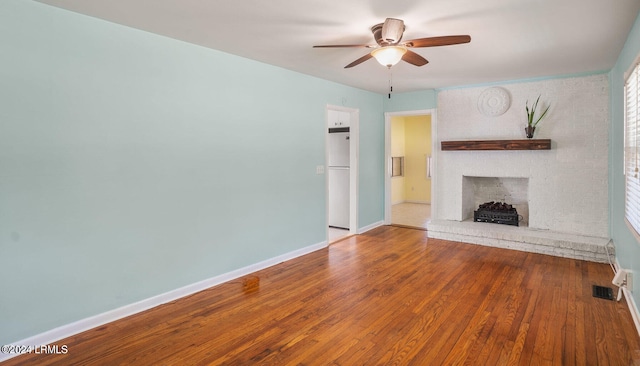 unfurnished living room featuring hardwood / wood-style flooring, ceiling fan, and a brick fireplace