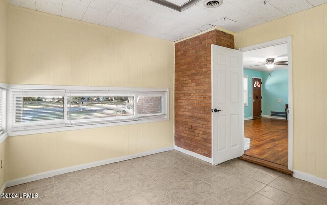 unfurnished room with a wealth of natural light, ceiling fan, and brick wall