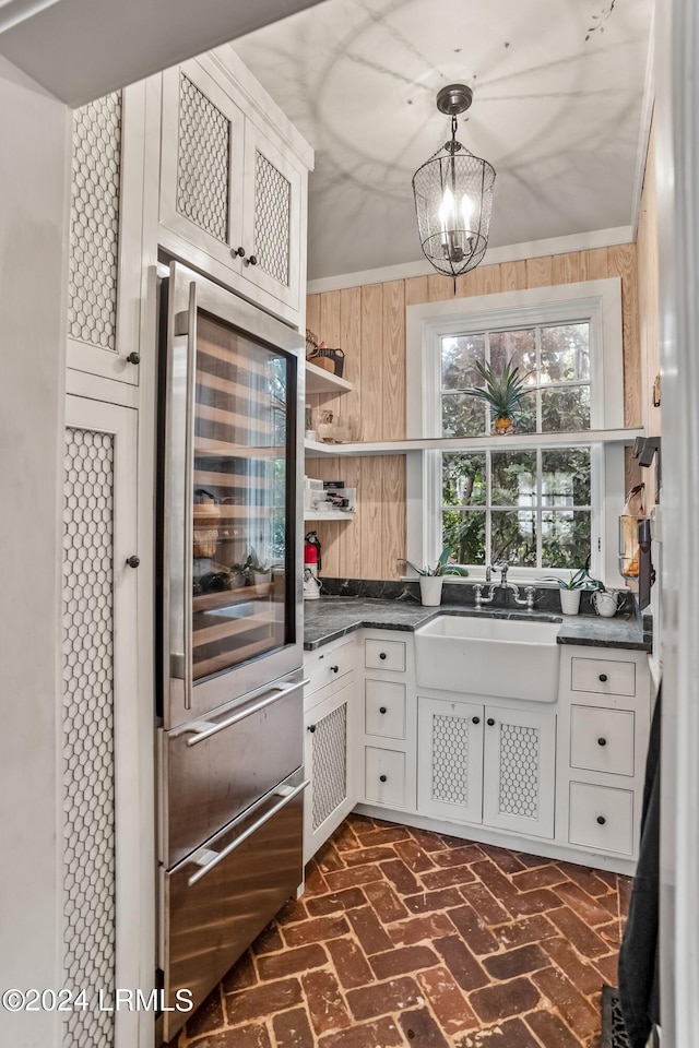 kitchen featuring sink, white cabinetry, hanging light fixtures, wooden walls, and beverage cooler