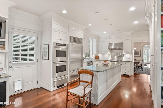 kitchen with a breakfast bar area, appliances with stainless steel finishes, light stone counters, ventilation hood, and a kitchen island