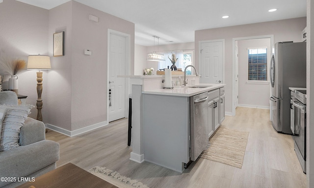 kitchen with sink, stainless steel appliances, light hardwood / wood-style floors, an island with sink, and decorative light fixtures