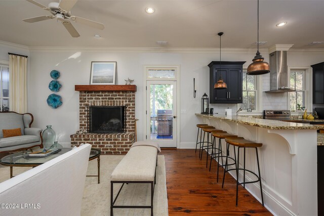 living room with crown molding, a brick fireplace, ceiling fan, and dark hardwood / wood-style flooring