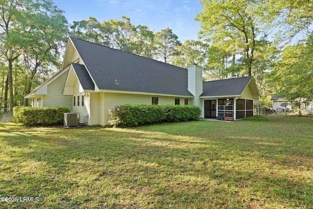 rear view of property with roof with shingles, a chimney, central AC unit, a sunroom, and a lawn