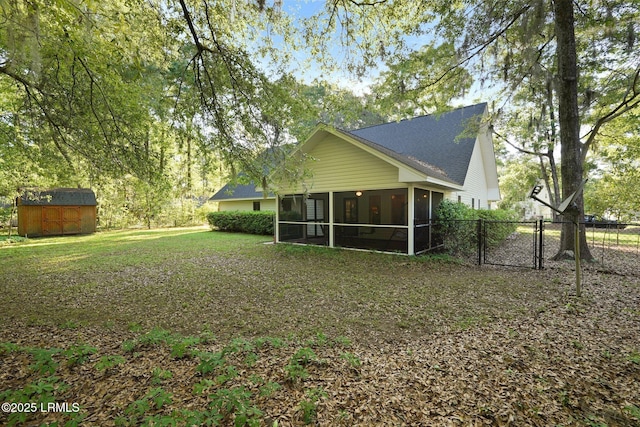rear view of house with a shingled roof, a sunroom, fence, a storage unit, and an outbuilding