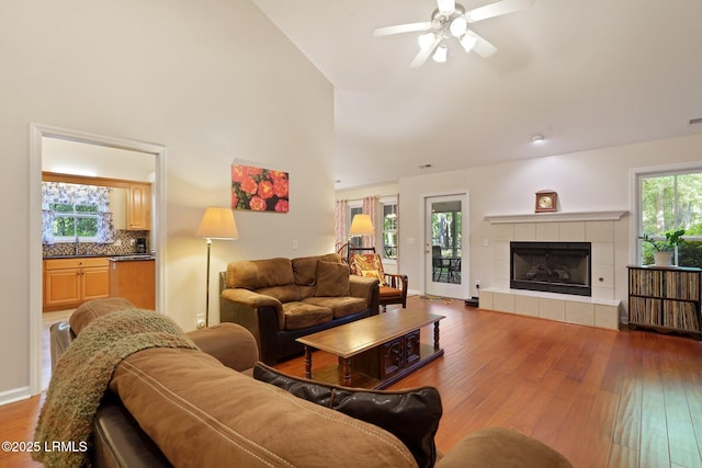 living room with baseboards, a tiled fireplace, a high ceiling, a ceiling fan, and wood-type flooring