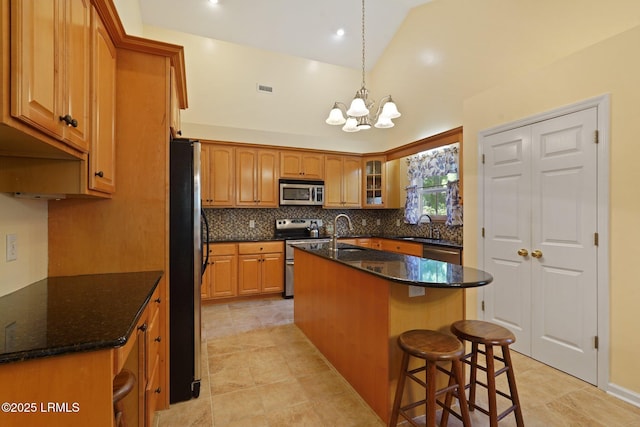 kitchen featuring tasteful backsplash, dark stone countertops, a kitchen island with sink, stainless steel appliances, and a notable chandelier